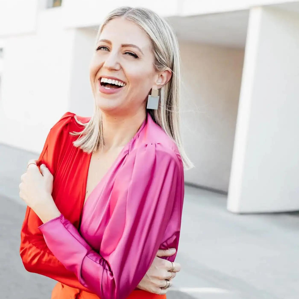 Fashion stylist Lindsay Albanese wearing a vibrant red and pink blouse, smiling joyfully outdoors.