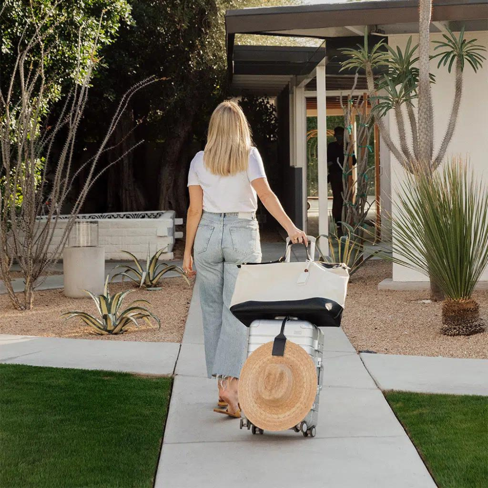 Woman in casual spring outfit with straw hat on suitcase, entering modern home with desert landscape.