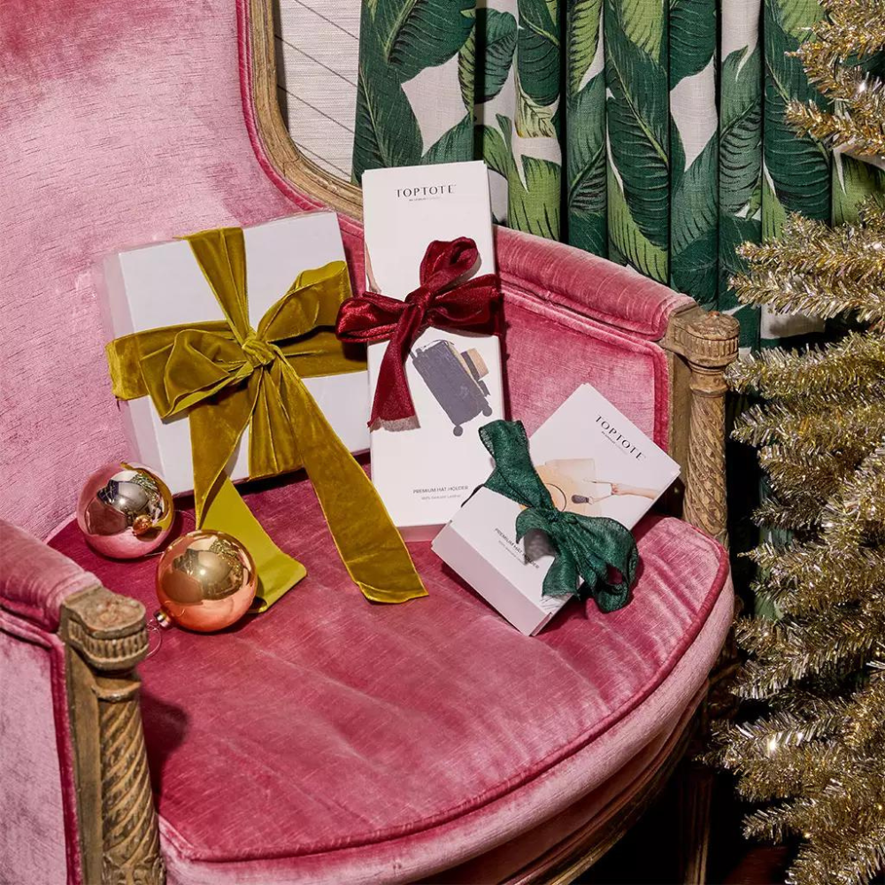 Stylish gifts under $150 beautifully wrapped with bows on a pink plush chair near Christmas decor.