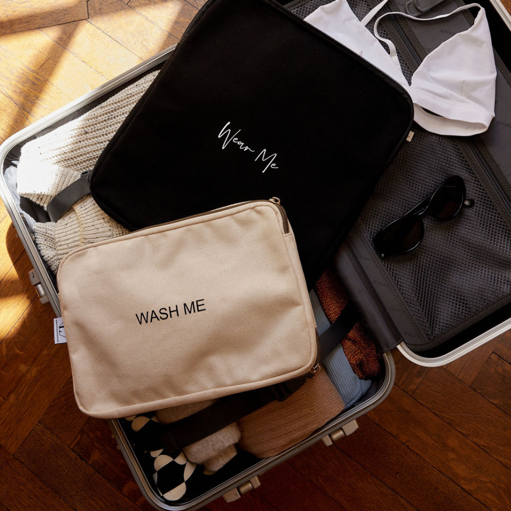 Open suitcase with Lindsay Albanese Two-Sided Travel Laundry Bag showing 'Wash Me' and 'Wear Me' compartments, ready for travel.