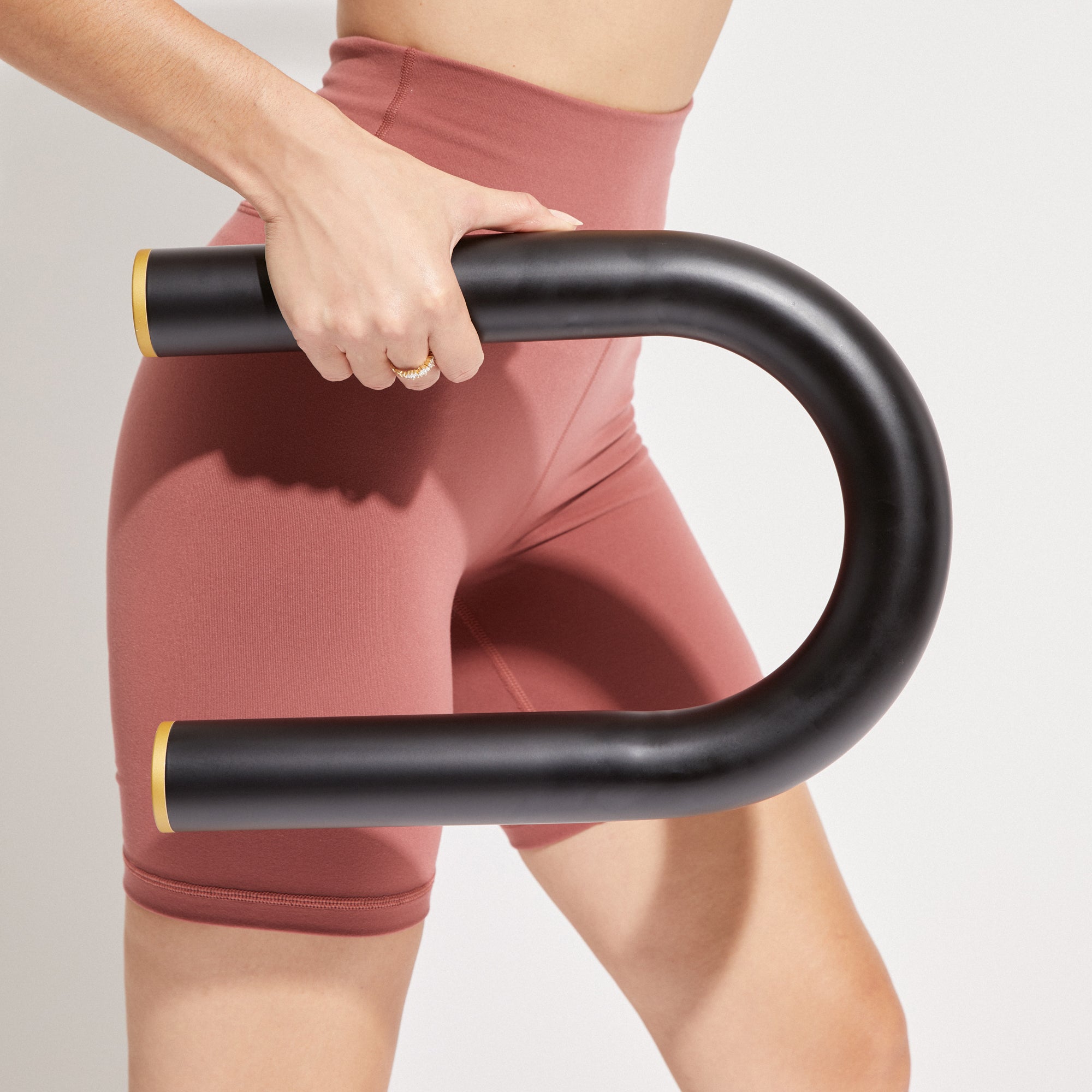 Person holding Ubarre Weighted Workout Bar against pink workout shorts, showcasing modern design and versatility in fitness equipment.
