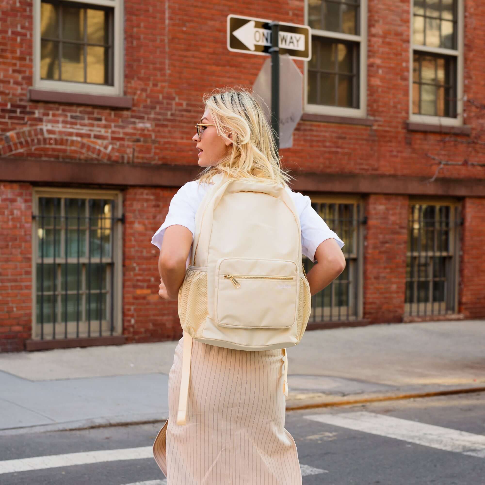 August Noa travel backpack in cream. Front view on a woman's back.