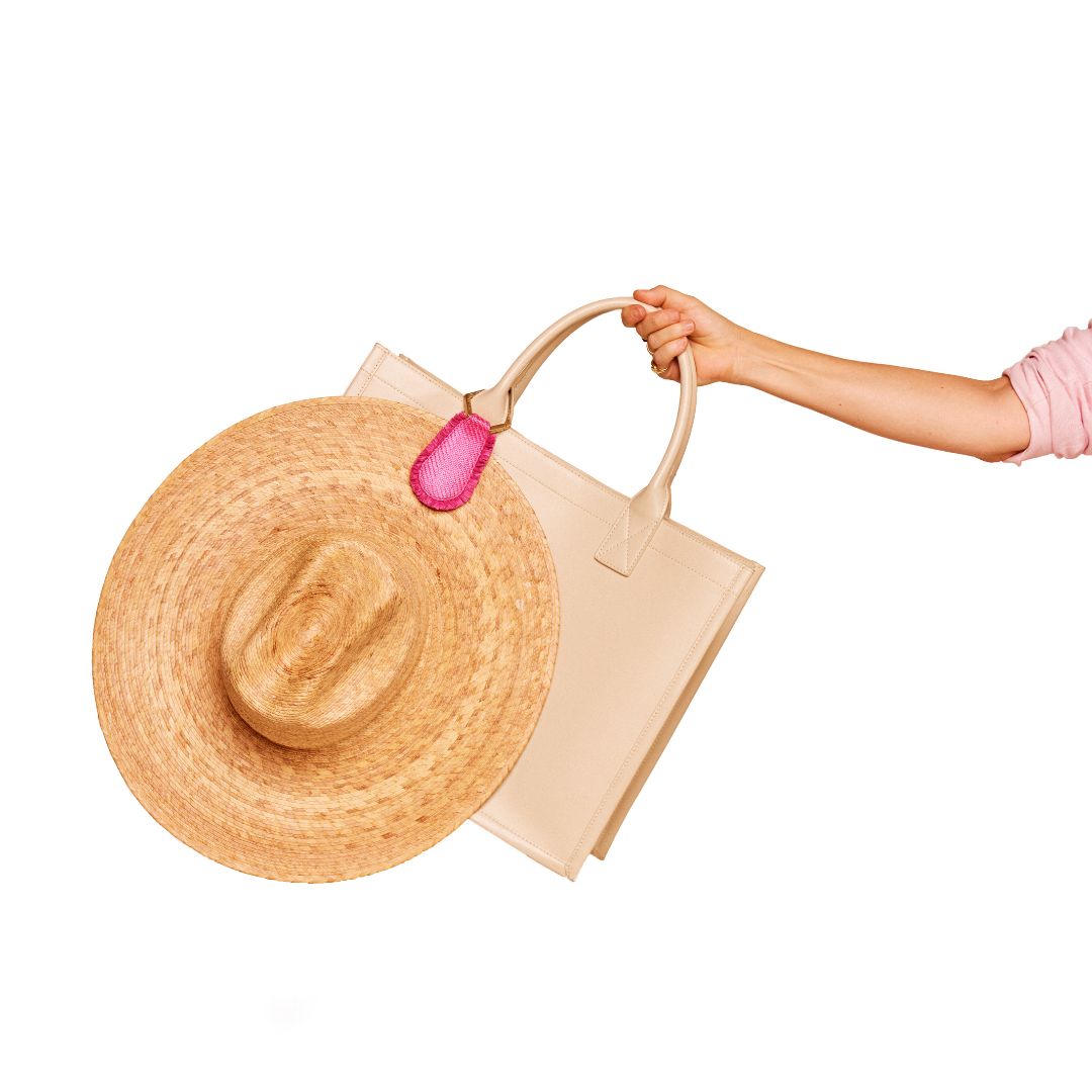 The Fray TOPTOTE Hat Clip with raffia trim holding a straw hat on a beige handbag.