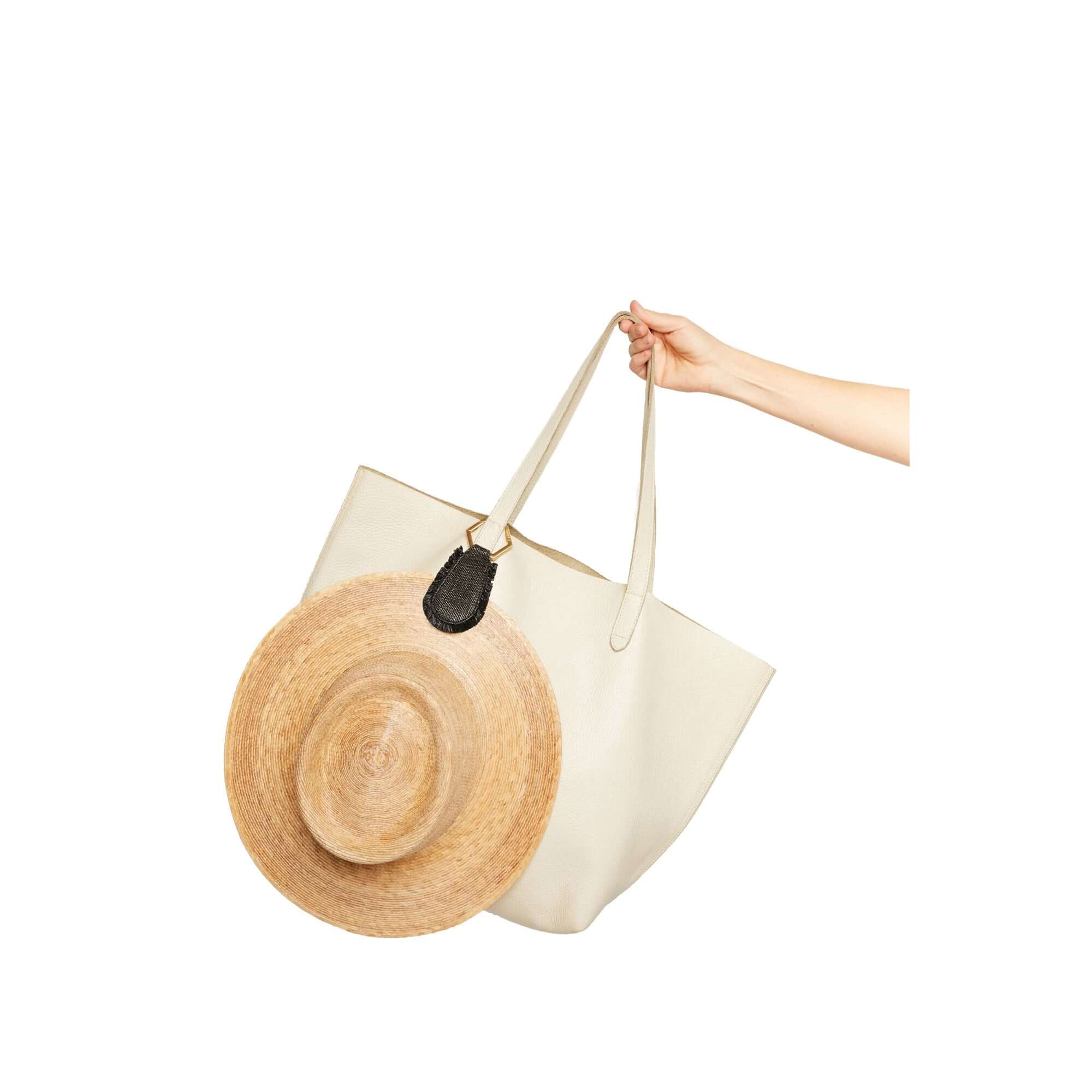 The Fray TOPTOTE hat clip with raffia trim holding a straw hat on a beige tote bag