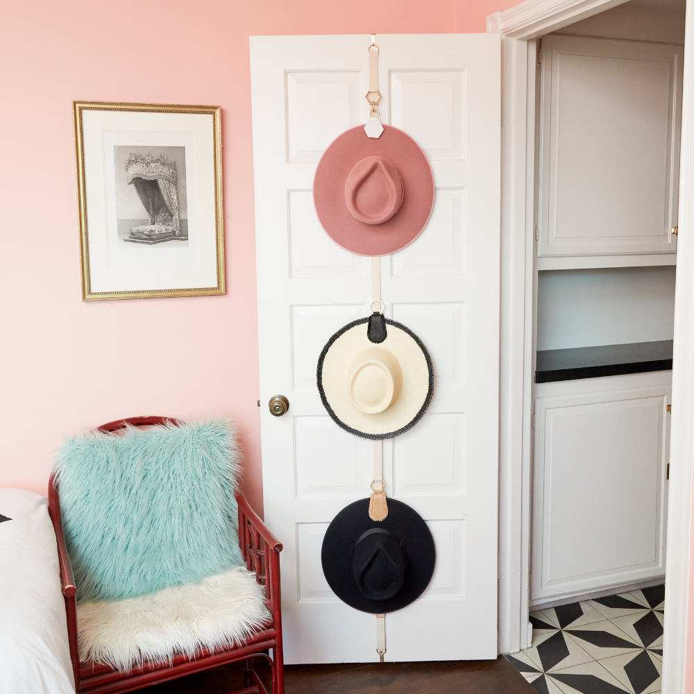 Hat organizer with three hats hung on a door using The Collector & TOPTOTE bundle in a room with pastel decor.