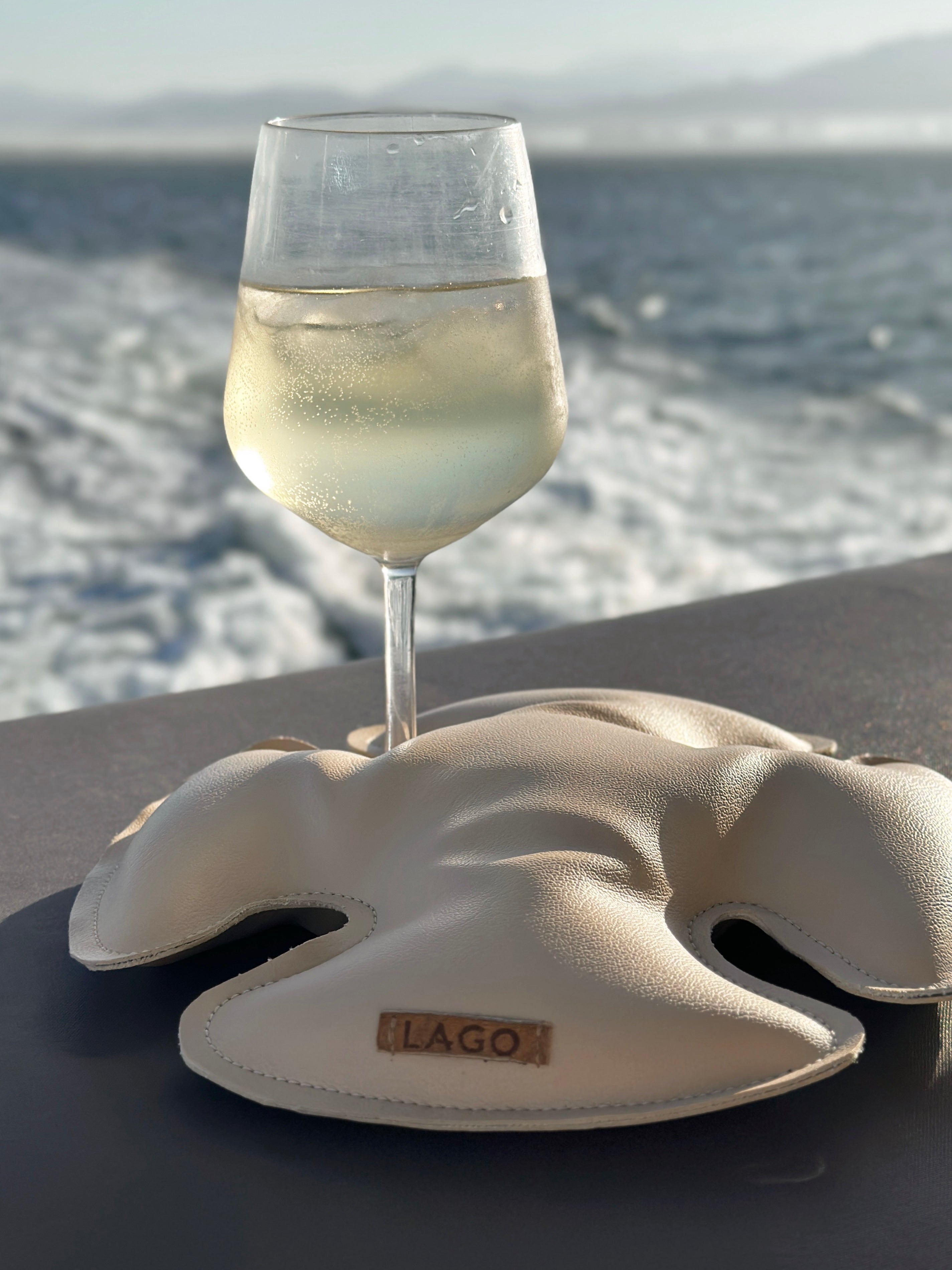 Lago 'Sand Dollar' Wine Holder securing a wine glass on a boat with scenic ocean view in the background.