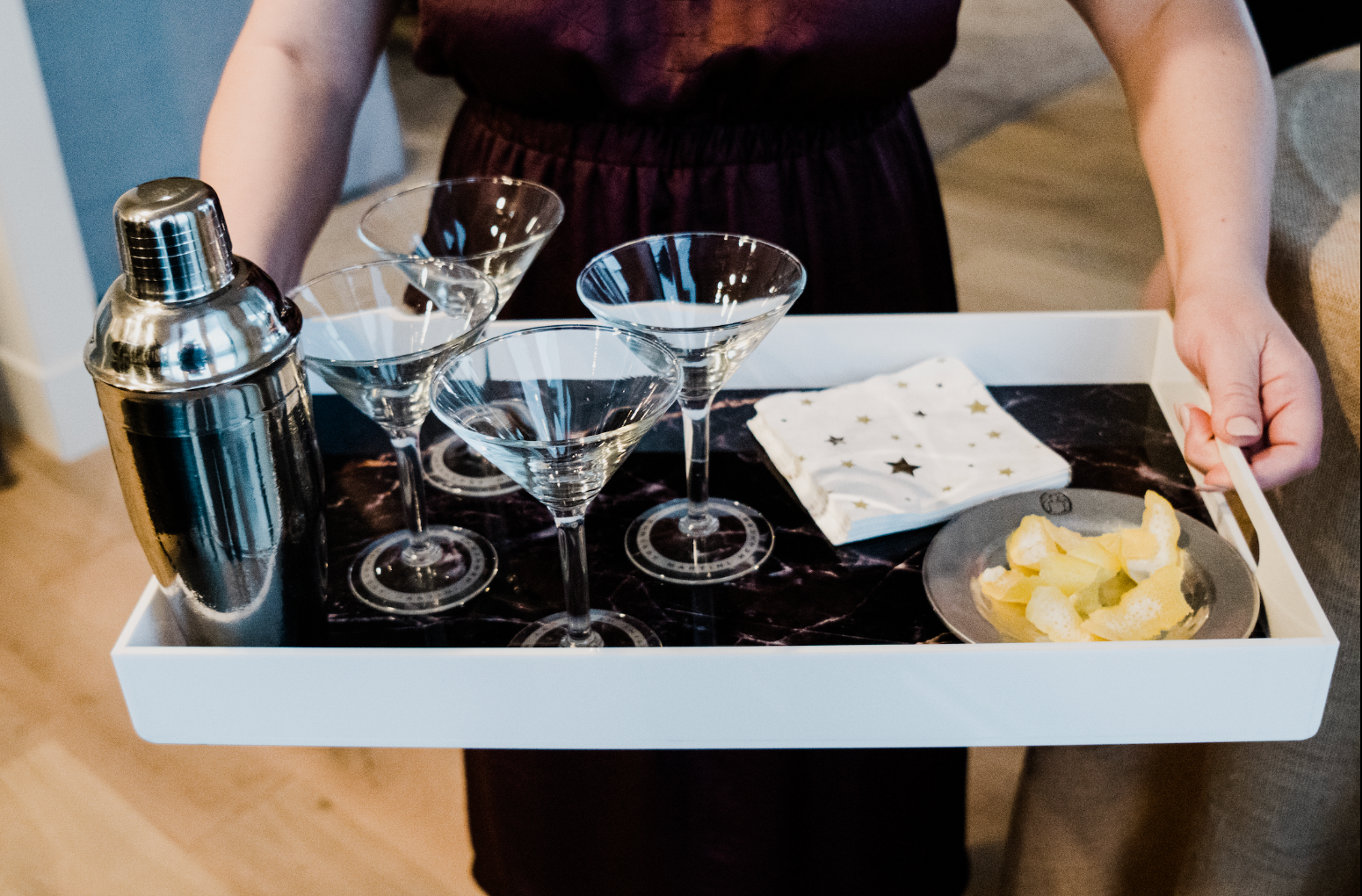 Person holding tray with martini glasses, cocktail shaker, napkins, and lemon garnish on black marble Rolling Stone reversible insert.