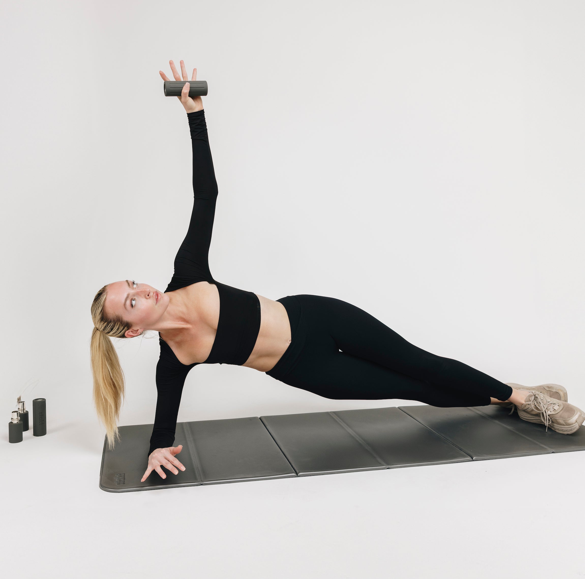 Woman using Stakt weight in iron on the Stake yoga mat with other weight options next to her. 