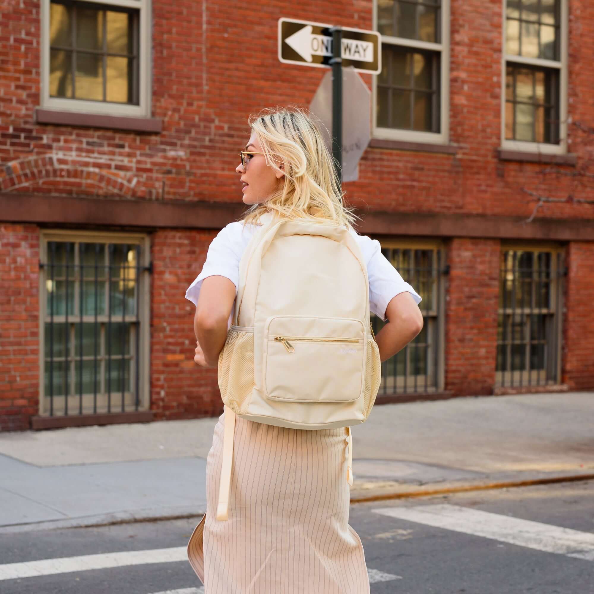 cream backpack made from recycled materials with gold hardware and lots of pockets including a protective sleeve for your laptop and trolley sleeve