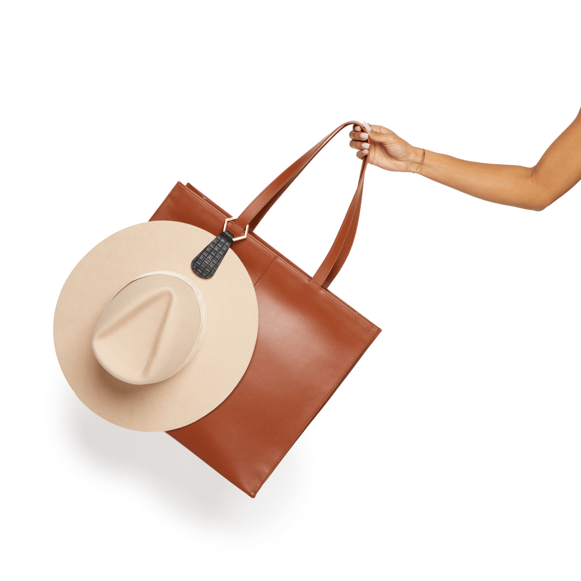 Hat attached to brown leather handbag with The Drop TOPTOTE hat clip showing hands-free travel convenience