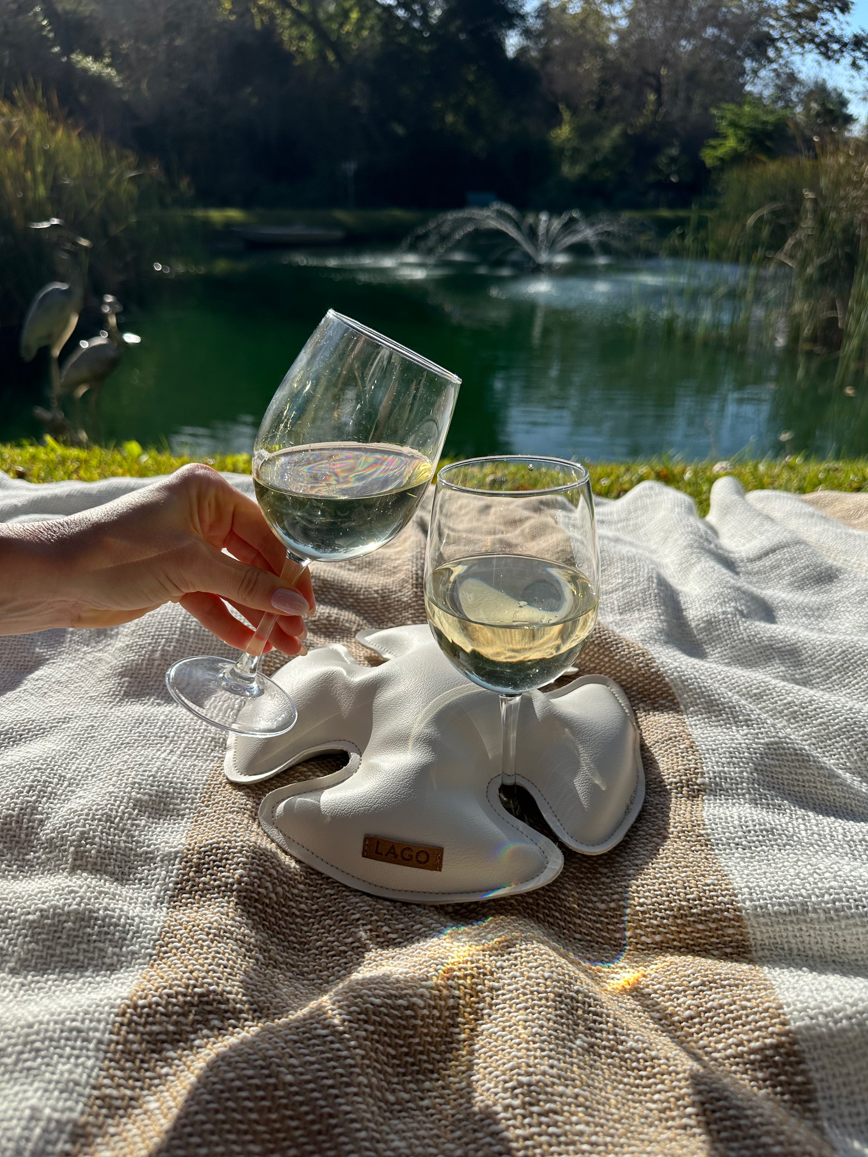 2 wine glasses secured with LAGO in sand dollar on a blanket by a lake.