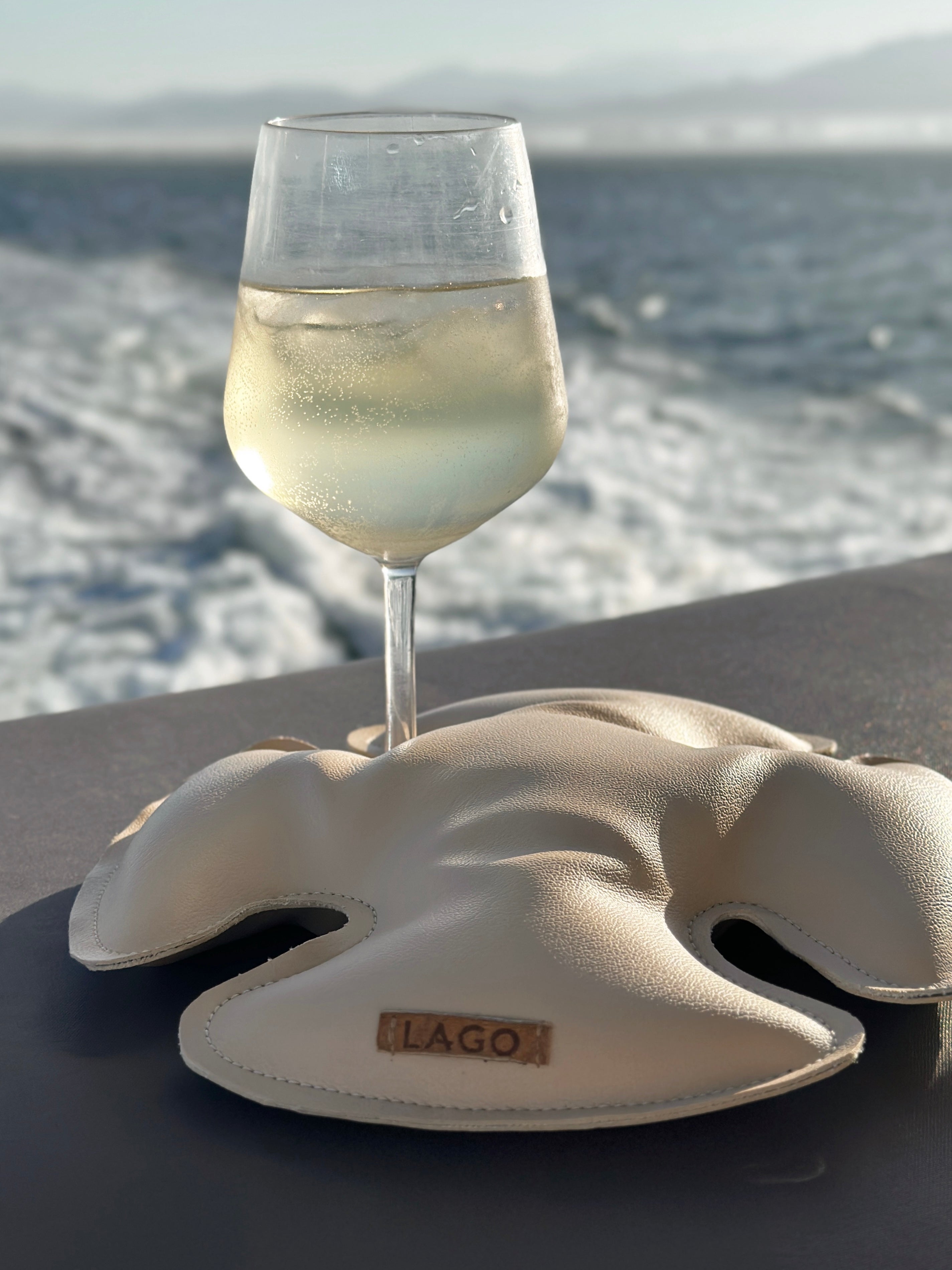 A wine glass secured by LAGO Sand Dollar on a table on a boat. 