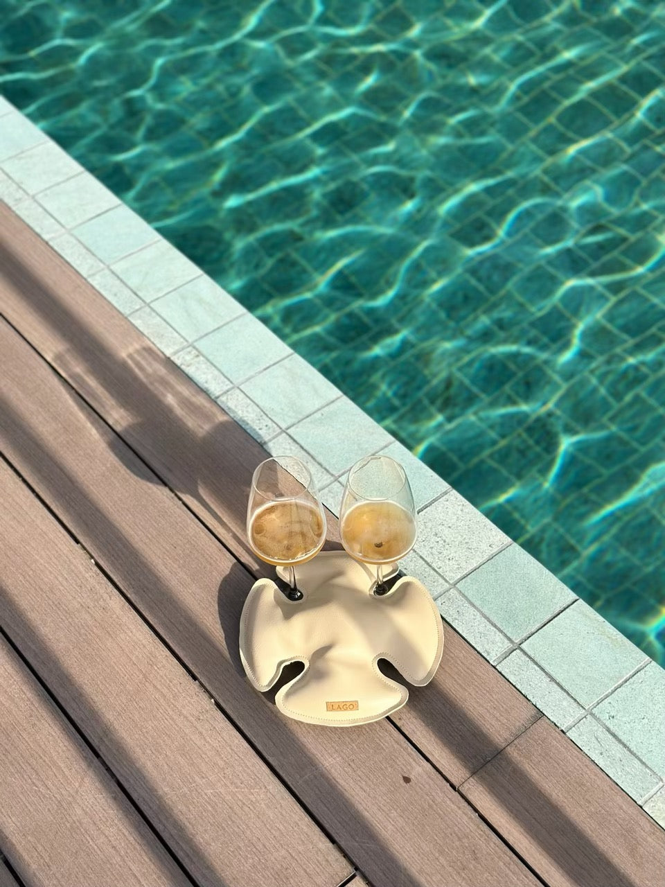 2 wine glasses secured by Lago sand dollar on a deck by the pool.